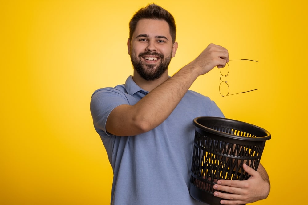 Young man holds a pair of glasses, preparing to drop them into a trash can after his iLASIK procedure
